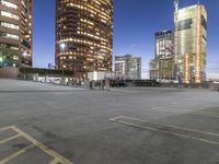 the empty parking lot is in front of tall buildings with bright lighting on them at night