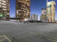 the empty parking lot is in front of tall buildings with bright lighting on them at night