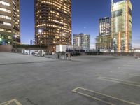 the empty parking lot is in front of tall buildings with bright lighting on them at night