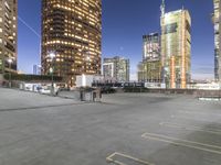 the empty parking lot is in front of tall buildings with bright lighting on them at night