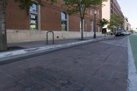 a brick walkway is near the street and sidewalk, near an old building that has windows