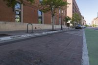 a brick walkway is near the street and sidewalk, near an old building that has windows