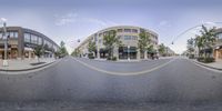 a 360 - lens photograph shows a wide street between buildings and shops at one end