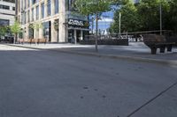 a park bench sitting on the side of the road on a sidewalk with buildings in the background