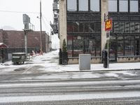 a traffic light on a snowy sidewalk in front of buildings and shops on a city street