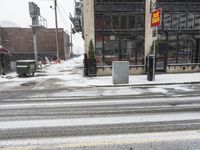 a traffic light on a snowy sidewalk in front of buildings and shops on a city street