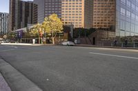 cars are driving along the empty city street near high rise buildings and tall glass office buildings