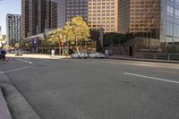 cars are driving along the empty city street near high rise buildings and tall glass office buildings