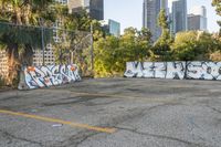 a view of city buildings in the background and some graffiti covered parking lot area with white walls and yellow lines on asphalt