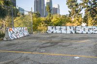 a view of city buildings in the background and some graffiti covered parking lot area with white walls and yellow lines on asphalt