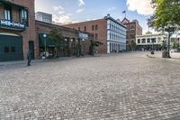 an old brick street in the city with people walking around it and buildings around it