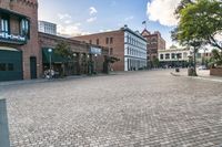 an old brick street in the city with people walking around it and buildings around it