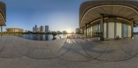 a circular mirror is showing people by the water and buildings in the background with reflection on the pavement