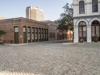 a city with a small brick street with parked cars and people walking down it in the distance