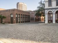 a city with a small brick street with parked cars and people walking down it in the distance