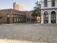 a city with a small brick street with parked cars and people walking down it in the distance