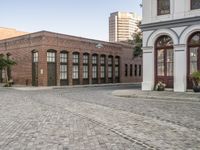 a city with a small brick street with parked cars and people walking down it in the distance