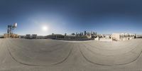 a view of a skateboard park in a large city setting, looking toward the sun