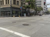 an intersection with empty street in front of tall buildings and trees across the street from each other