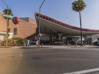 an intersection with a large building and parked cars in front of it and palm trees