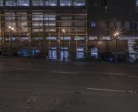 a building with glass fronting on an empty road with street lights in the dark