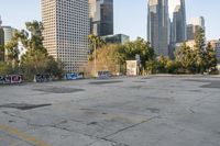 an empty parking lot with graffiti covered walls in front of tall buildings and trees in the distance