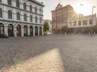 the sun is setting in the middle of an empty street with large buildings around it