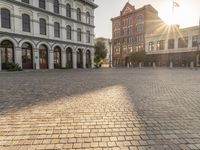 the sun is setting in the middle of an empty street with large buildings around it