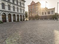 the sun is setting in the middle of an empty street with large buildings around it