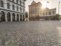 the sun is setting in the middle of an empty street with large buildings around it