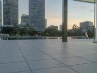 the walkway at the park leads to a lake and buildings in the background as evening falls