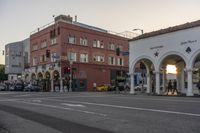 a street intersection with people and a building on both sides of the street at sunset