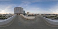 a picture of a ramp going up to a building with buildings in the background in a panorama lens