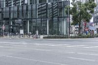 an empty city street with a large building and bicycles parked beside it in the background