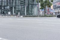 an empty city street with a large building and bicycles parked beside it in the background