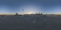 two cars parked in an empty parking lot with a city skyline behind them with a cloudy sky