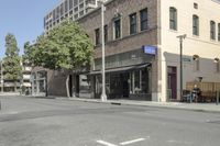 people walking on a street past tall buildings near a cross walk with tables and chairs in front of it
