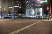 an empty street lined with tall buildings at nighttime / and an traffic light turned on to red