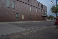 an empty street next to a tall brick building with windows and bushes on the sidewalk