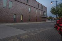 an empty street next to a tall brick building with windows and bushes on the sidewalk