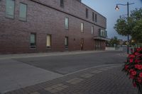 an empty street next to a tall brick building with windows and bushes on the sidewalk