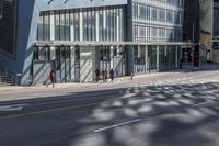 people walking on the sidewalk in front of a building with lots of glass doors and windows