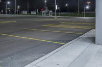 there is a parking lot with a couple lights on at night time, and no cars on the street