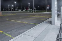 there is a parking lot with a couple lights on at night time, and no cars on the street