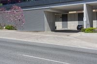 a car is parked in front of an office building on a street corner with a concrete parking garage and flowering trees on the sidewalk