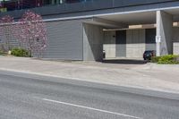 a car is parked in front of an office building on a street corner with a concrete parking garage and flowering trees on the sidewalk