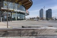 an empty parking lot with benches and wooden posts in front of it in front of tall buildings