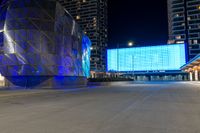 blue and silver building sitting next to an empty street at night time near other large buildings