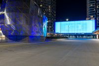 blue and silver building sitting next to an empty street at night time near other large buildings