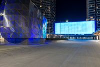 blue and silver building sitting next to an empty street at night time near other large buildings